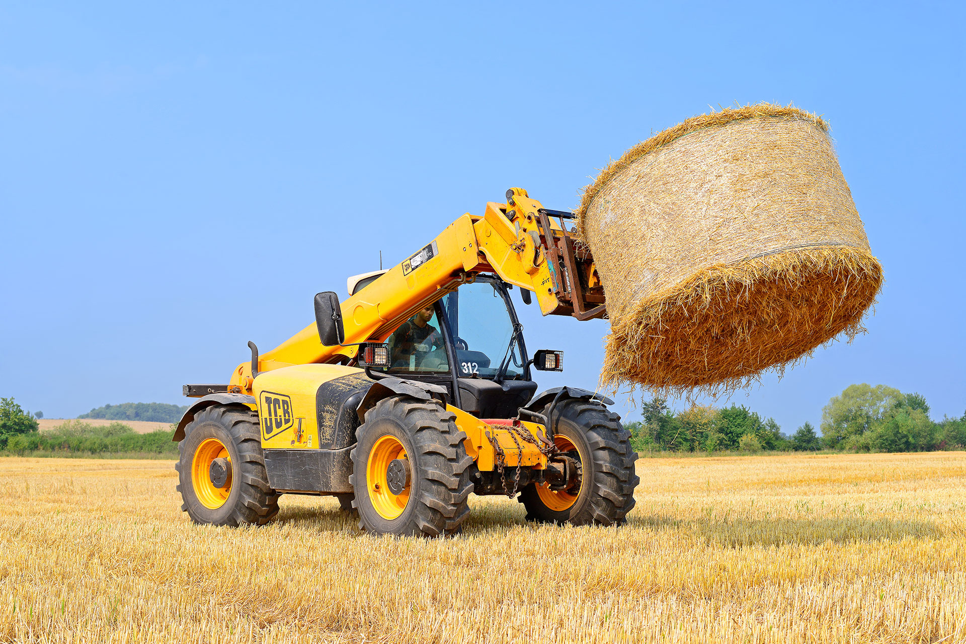 Telehandler in a field with a round bale.